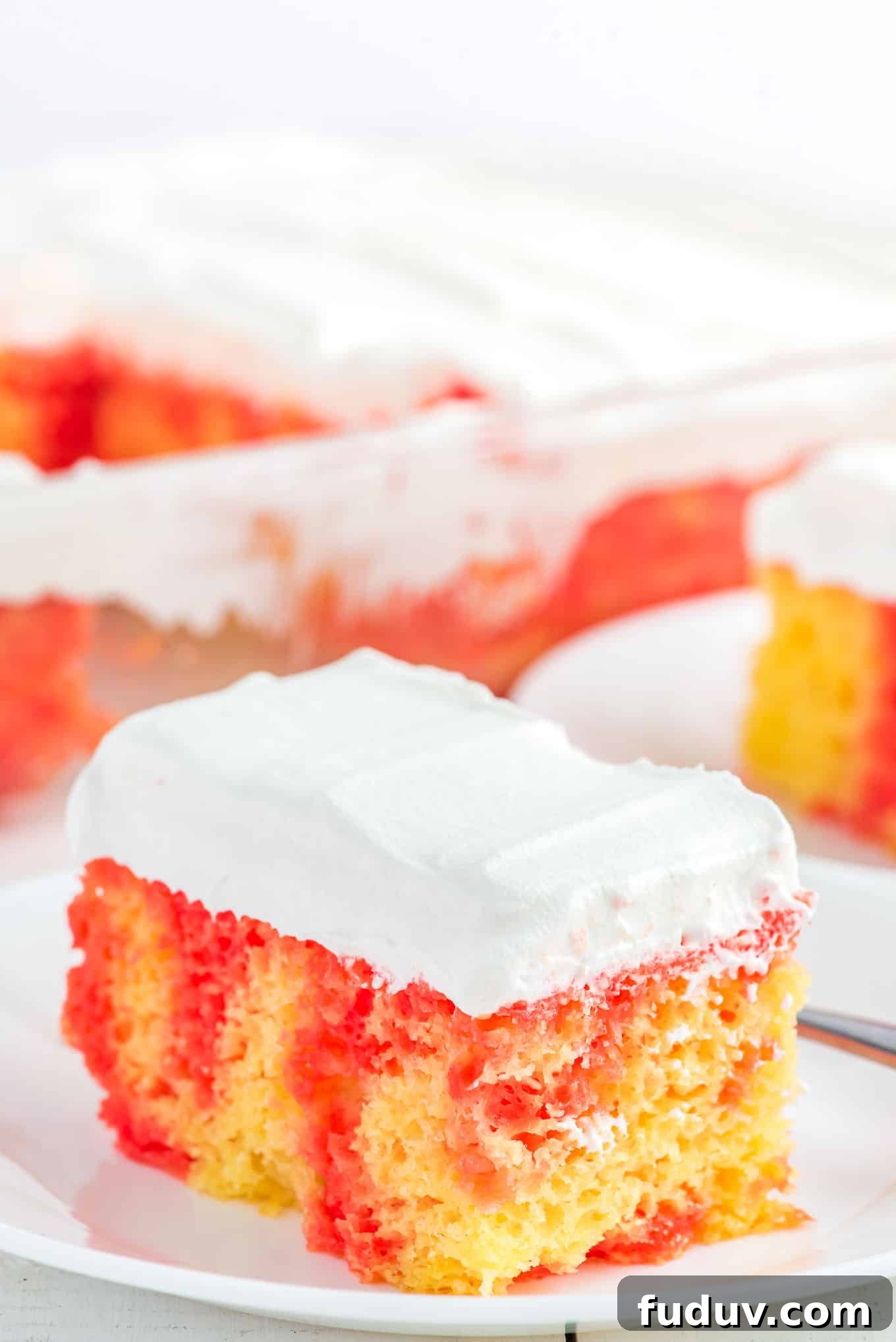 A square of strawberry and lemon cake on a plate topped with whipped cream frosting.