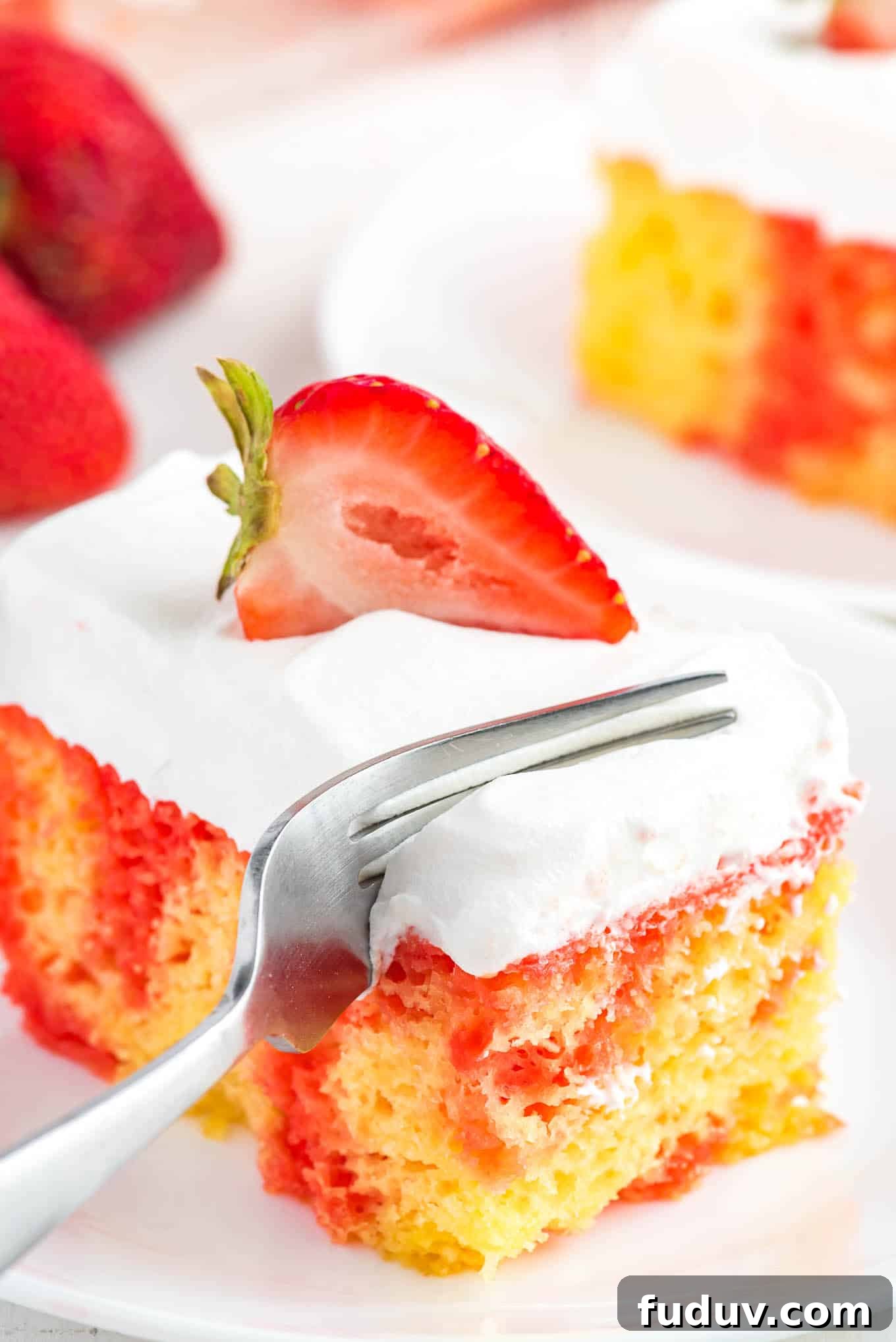 A fork cutting into a corner of a piece of strawberry lemonade poke cake.
