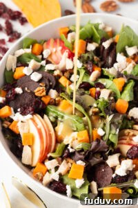 30+ Delicious Recipes to Transform Leftover Turkey 5 A salad in a white bowl featuring mixed greens, apple slices, cooked sweet potatoes, beets, nuts, dried cranberries, and crumbled cheese. A creamy dressing is being poured over the top. Ingredients are scattered around the bowl.