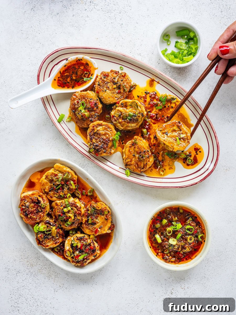 Crispy Homemade Dumpling Rolls: Step-by-Step Recipe 9 Two oval plates of stuffed eggplant rounds topped with chili oil and chopped green onions, with a bowl of dipping sauce and a small bowl of green onions nearby; a hand holds chopsticks picking up a piece.