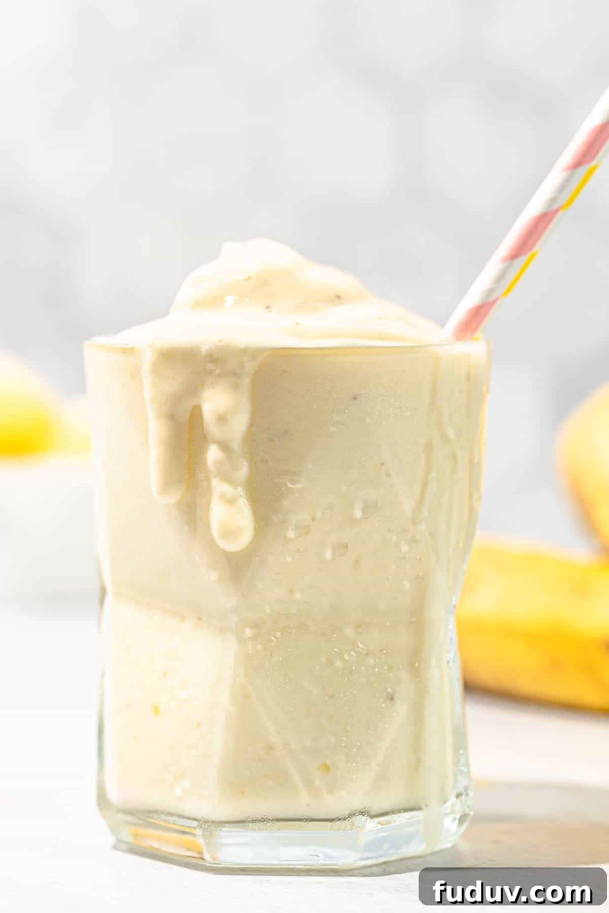 pineapple banana smoothie in short glass with pink straw
