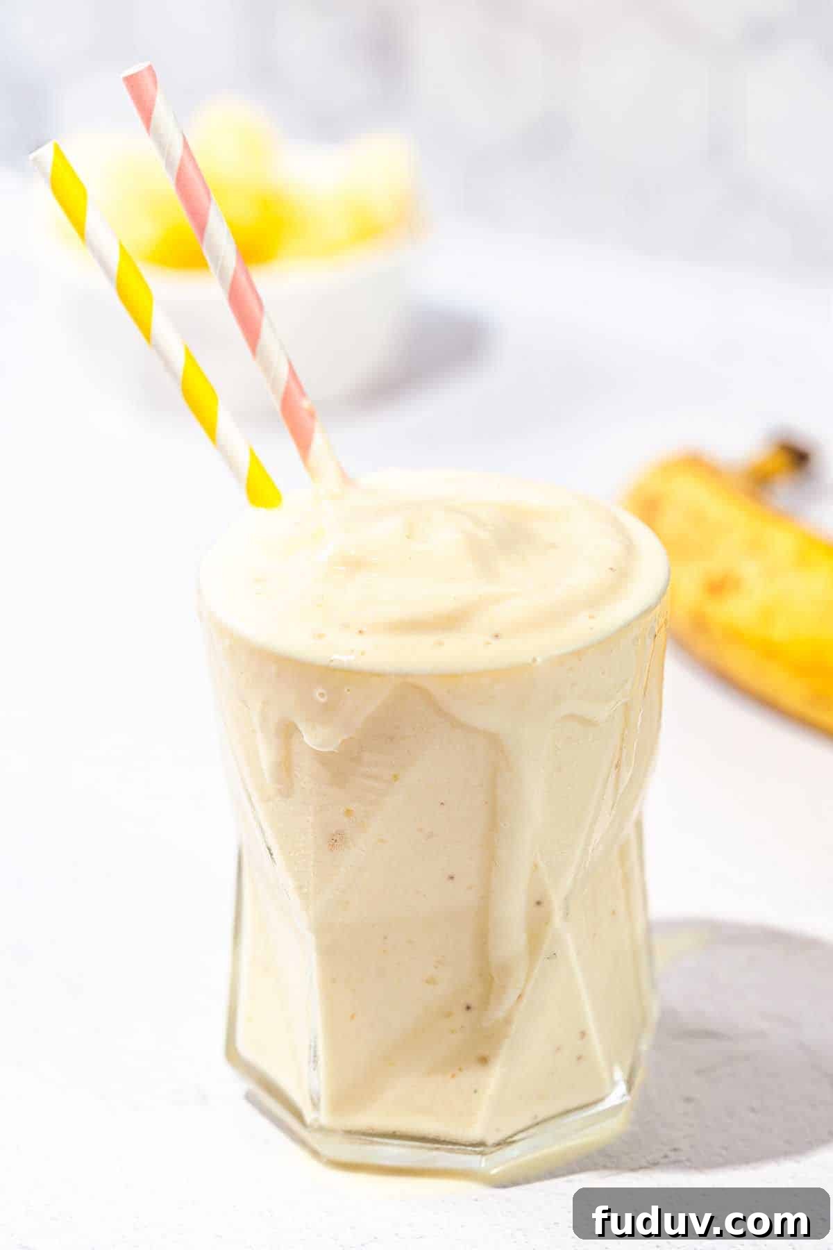 smoothie in a glass with two straws and banana in background