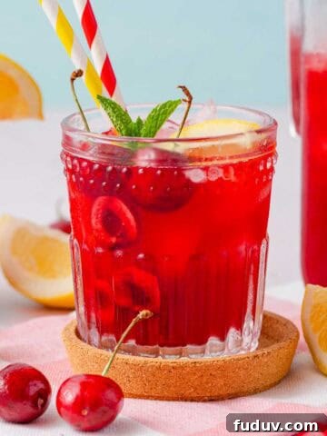 cherry lemonade in glass with two straws and cherry garnishes.