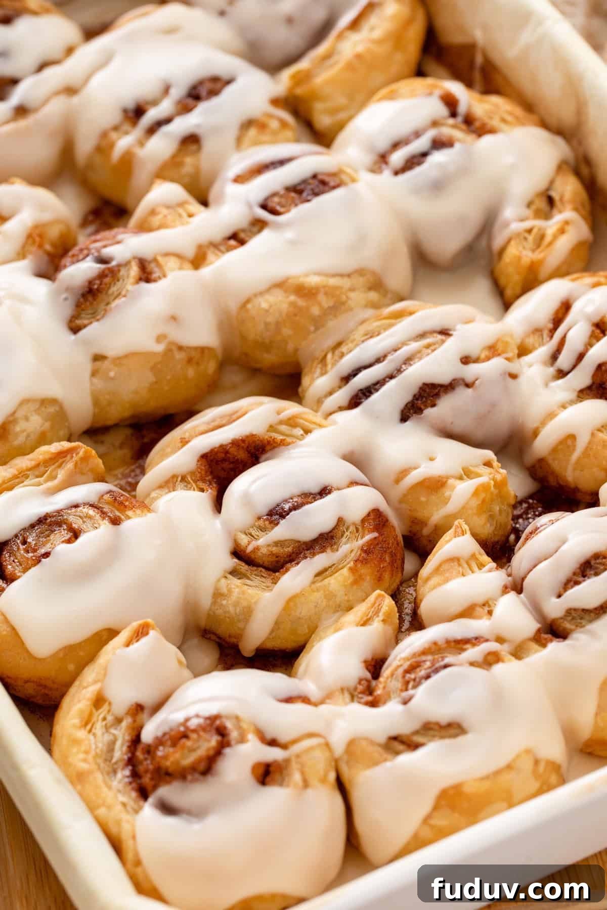 Close up of glazed puff pastry cinnamon rolls in a white baking pan.