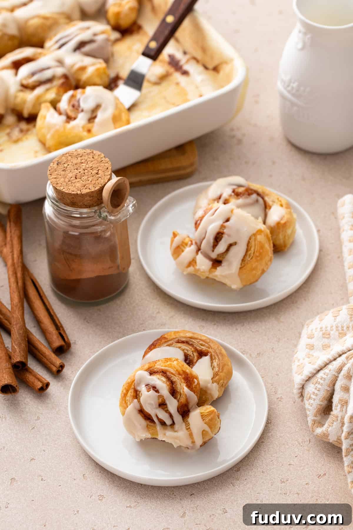 Two white plates of puff pastry cinnamon rolls on a countertop.