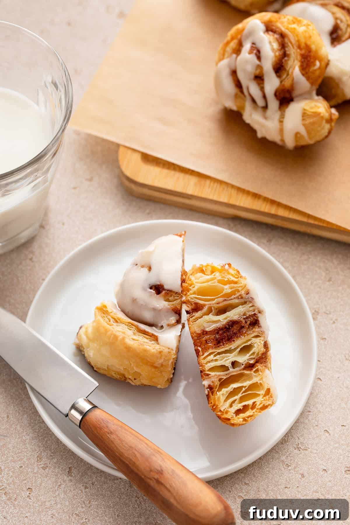 Puff pastry cinnamon roll cut in half on a white plate.