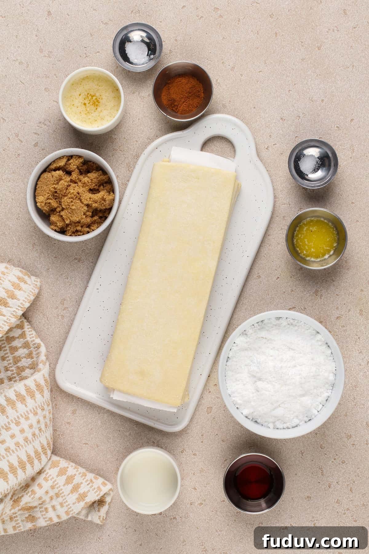Ingredients for puff pastry cinnamon rolls arranged on a beige countertop.