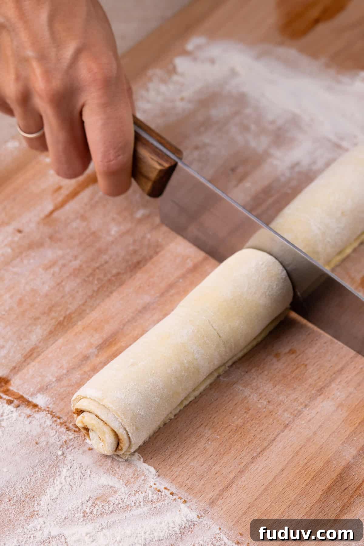 Knife cutting a roll of puff pastry cinnamon rolls.