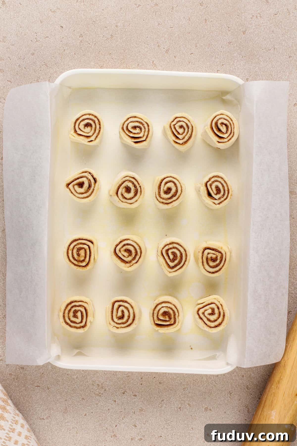 Unbaked puff pastry cinnamon rolls in a white baking pan.