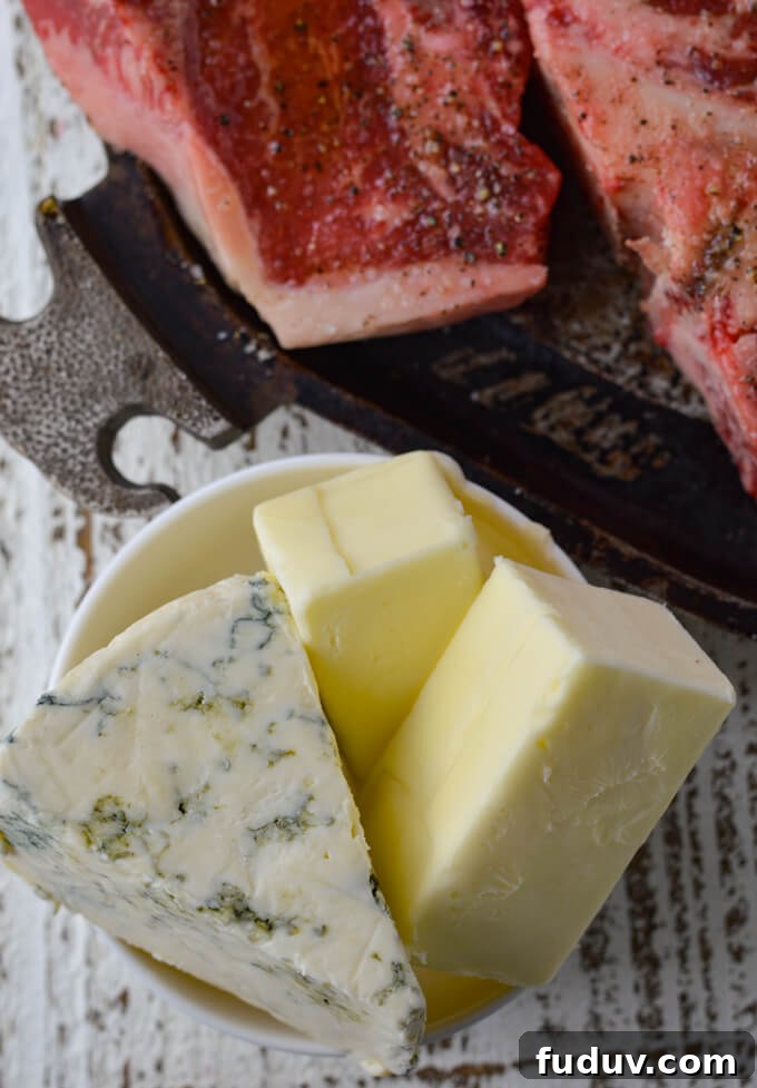 A small white bowl holding a chunck of blue cheese and 2 half sticks of butter. This sits next to a pan where you can see a partial t-bone steak.