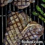 Two cooked t-bone steaks are on the grill with crisscross grill marks on them. Asparagus sits next to them on the grill.