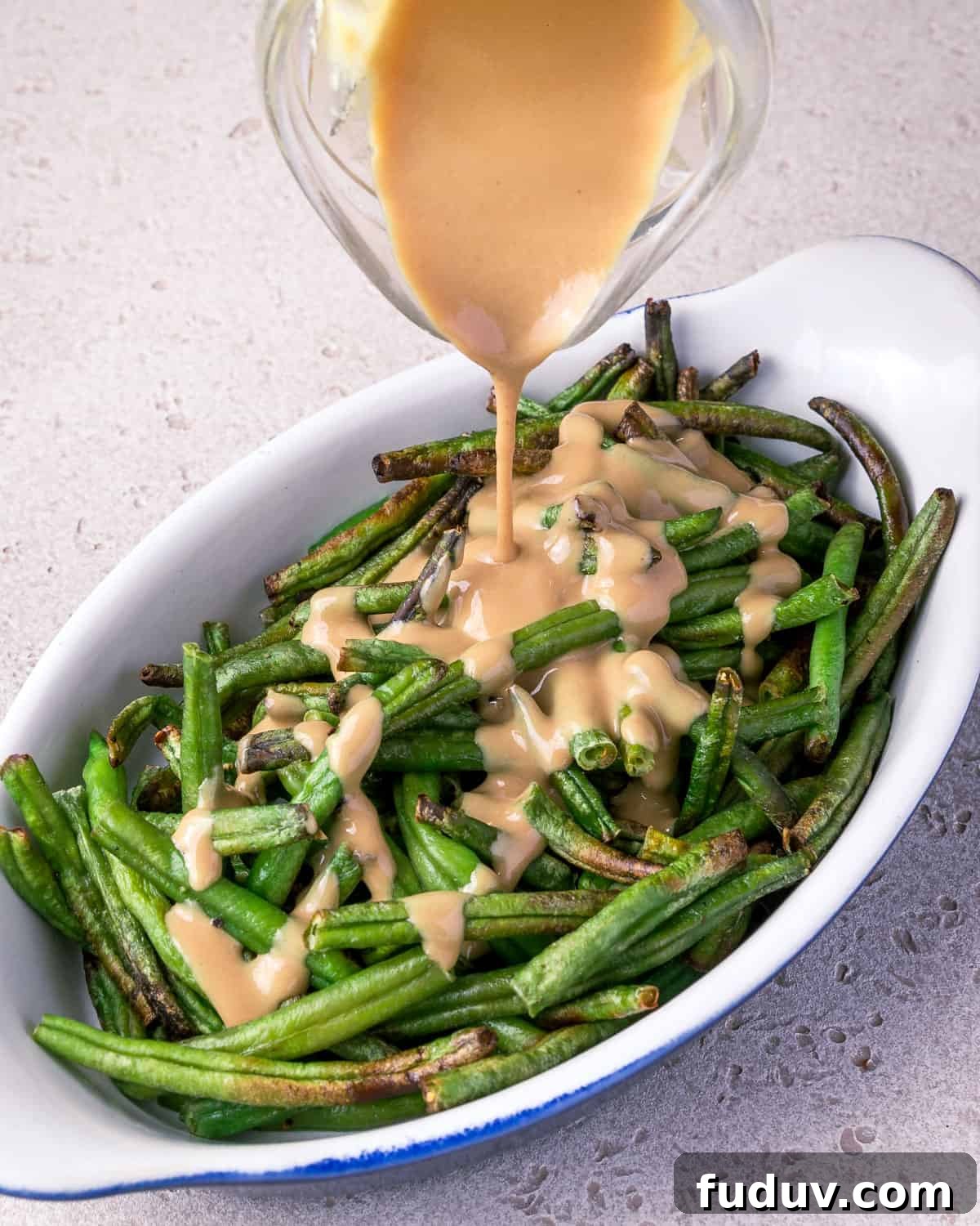 Crispy Air-Fried Frozen Green Beans with Creamy Tahini Sauce 13 Photo showing tahini sauce being poured on top of a dish of air fried frozen green beans.