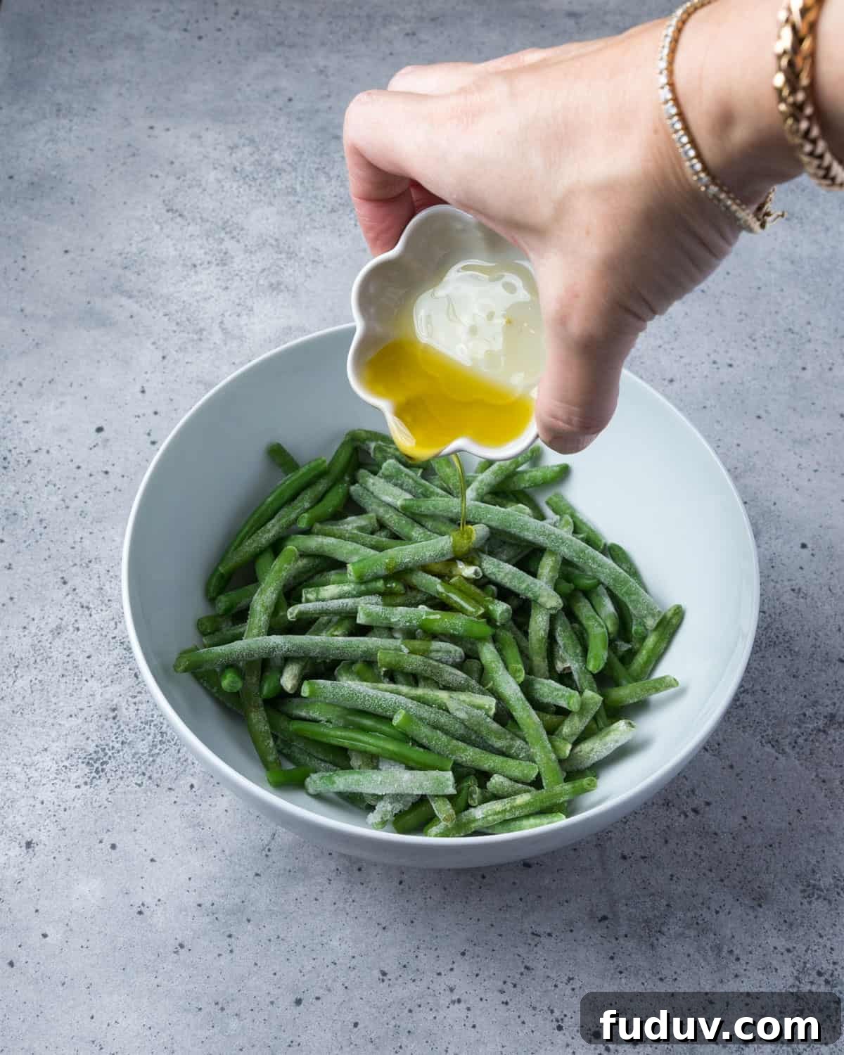 Crispy Air-Fried Frozen Green Beans with Creamy Tahini Sauce 7 Photo showing olive oil being poured onto a bowl of frozen green beans.
