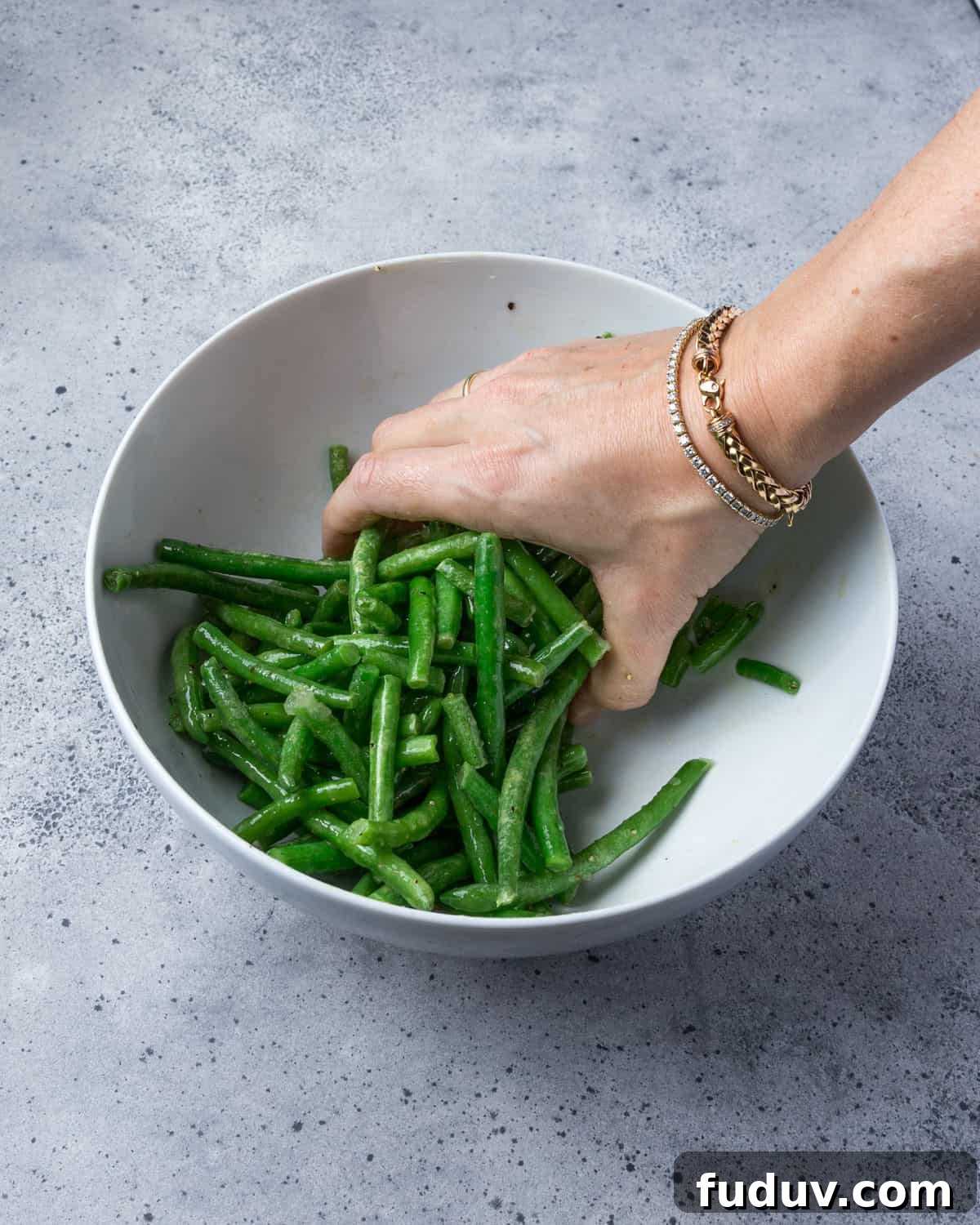 Crispy Air-Fried Frozen Green Beans with Creamy Tahini Sauce 9 Photo showing green beans being mixed with the oil and seasonings in a bowl.