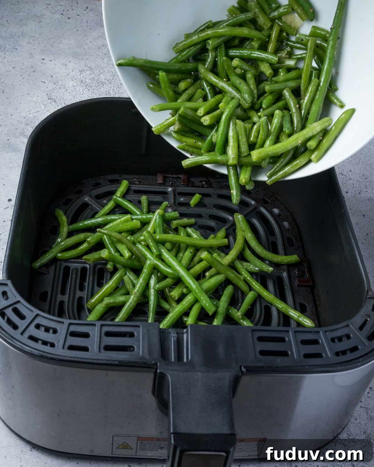 Crispy Air-Fried Frozen Green Beans with Creamy Tahini Sauce 10 Photo showing seasoned green beans being added to the air fryer.
