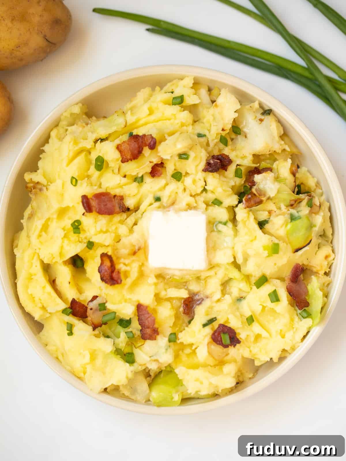 Colcannon in serving dish topped with a pat of butter and bacon.