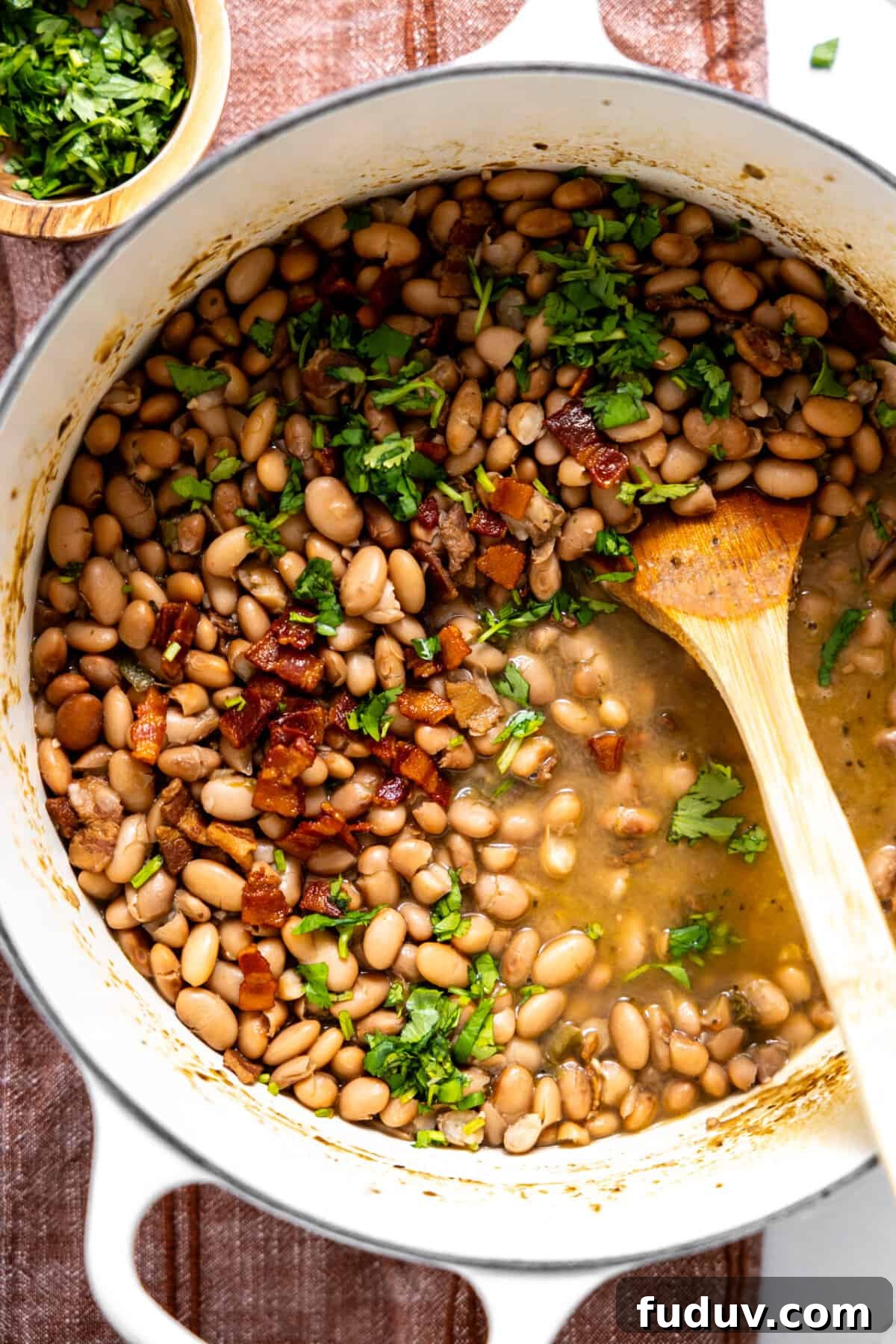 Pot of charro beans topped with cilantro and crispy bacon.