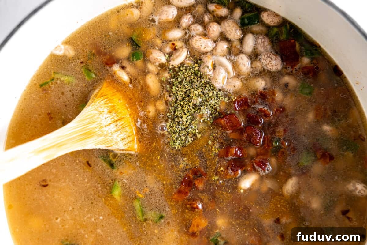 Dutch oven filled with broth, pinto beans, bacon, and seasonings.