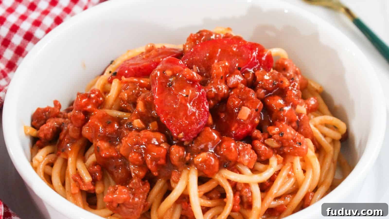 A bowl of spaghetti topped with a rich meat sauce placed on a red and white checkered tablecloth.