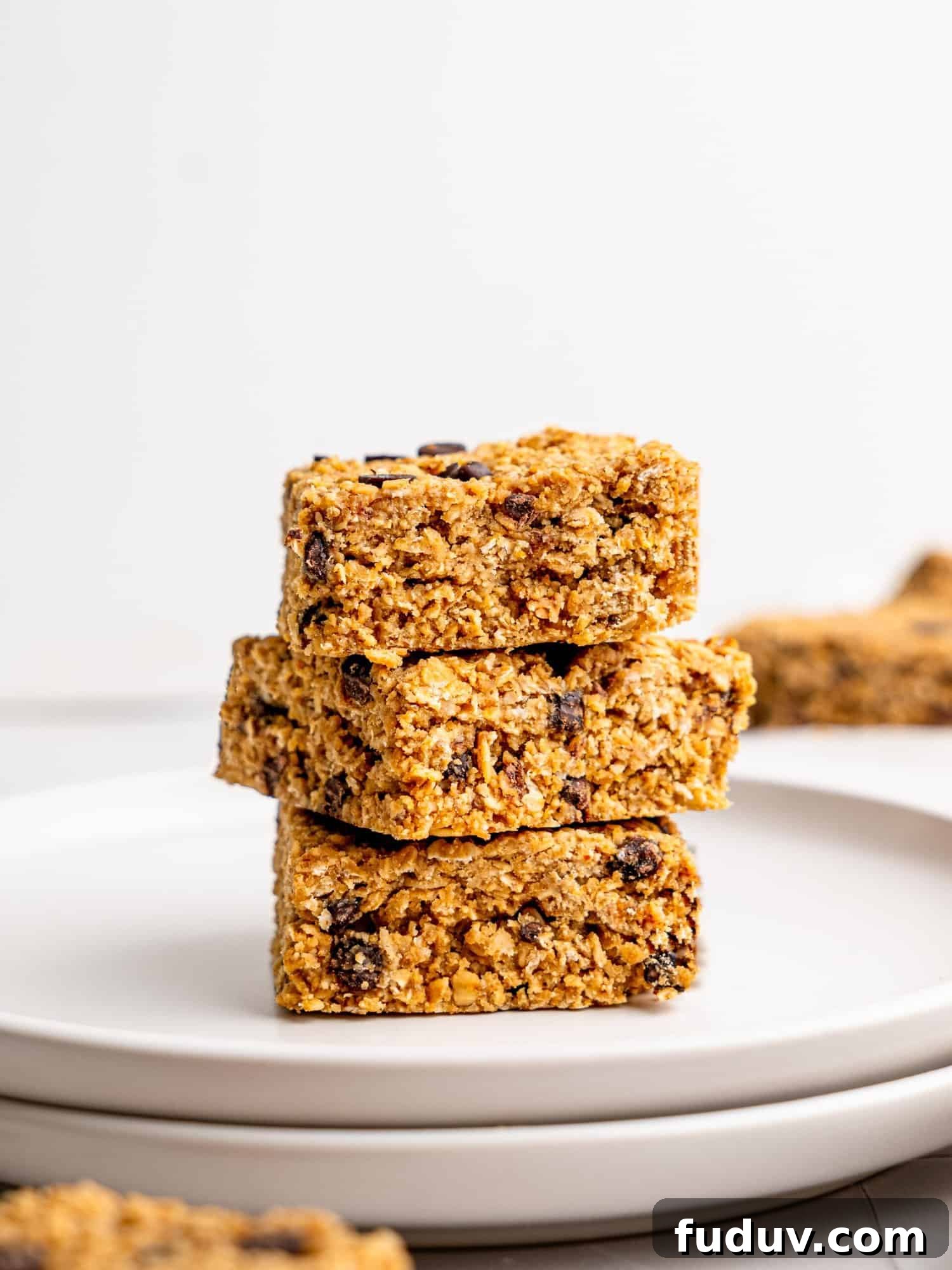 Three chocolate chips flapjacks stacked on top of each other on a white plate.