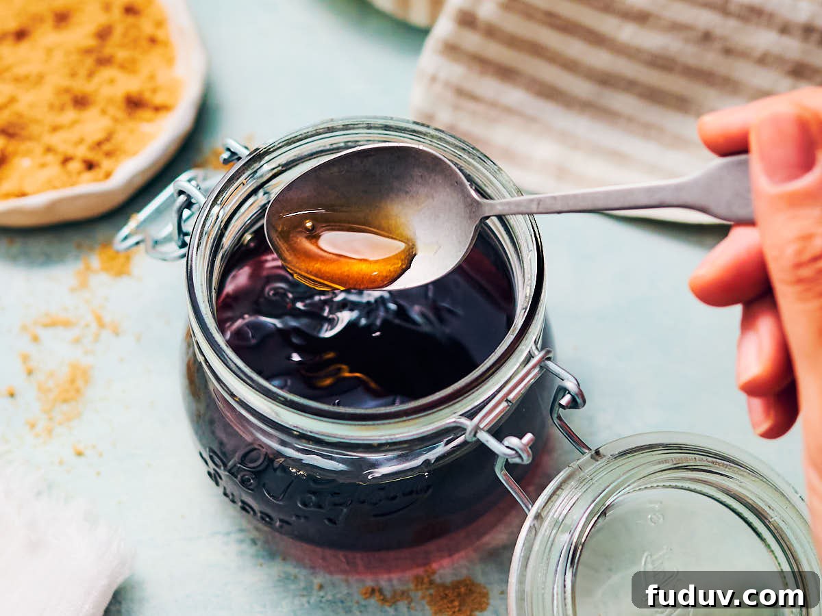 A spoon scooping out brown sugar simple syrup from a glass jar.