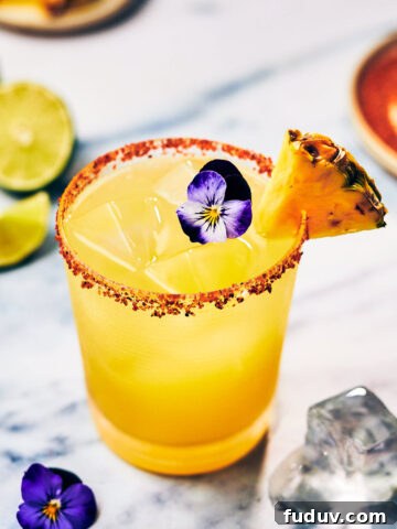 Spicy Pineapple Margarita in a glass with tajin salt rim.