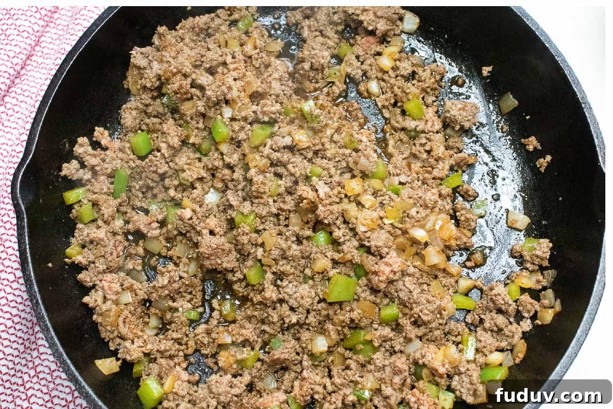 Cooked ground beef, diced onions and bell peppers in a cast iron skillet.