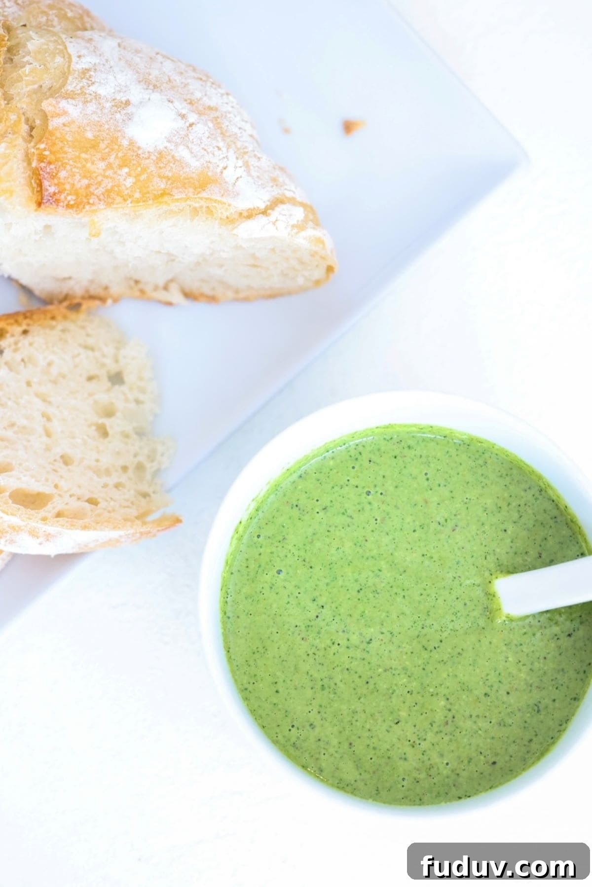 Pesto in a white bowl and two slices of sourdough bread on a white plate.