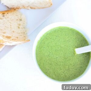 Pesto in a white bowl with a white spoon and a plate of sourdough to the top left of it.