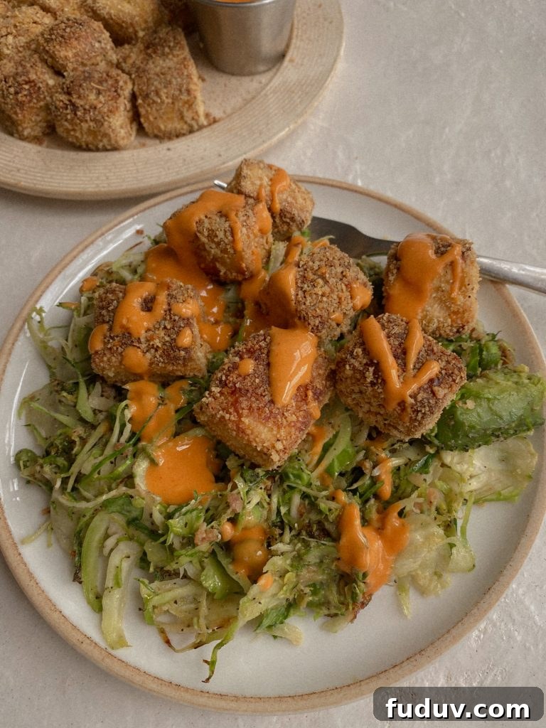Crispy Baked Gluten-Free Tofu Nuggets: Crunchy Oven Recipe 3 crispy baked tofu on shaved brussels sprouts with drizzle of buffalo sauce on white plate with fork