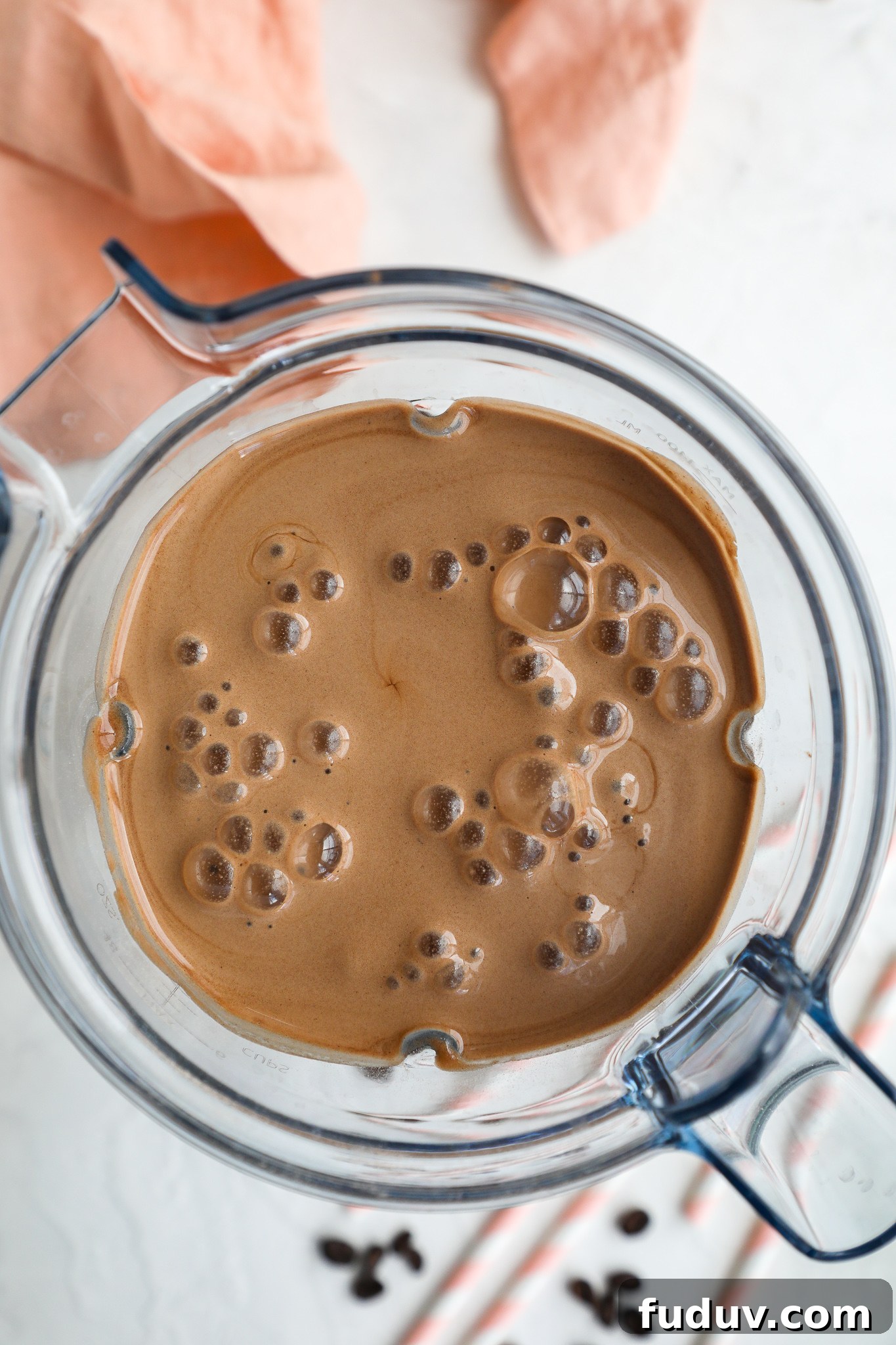 Creamy Mocha Protein Smoothie Recipe for Energy and Muscle Recovery 4 A mocha protein smoothie in a blended surrounded by a pink napkin and coffee beans