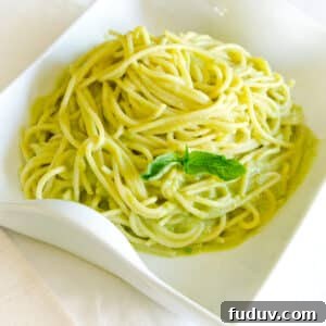 Creamy Avocado Pasta Recipe with Lemon and Parmesan 3 A white dish with spaghetti noodles in a creamy sauce with a sprig of fresh basil on it.