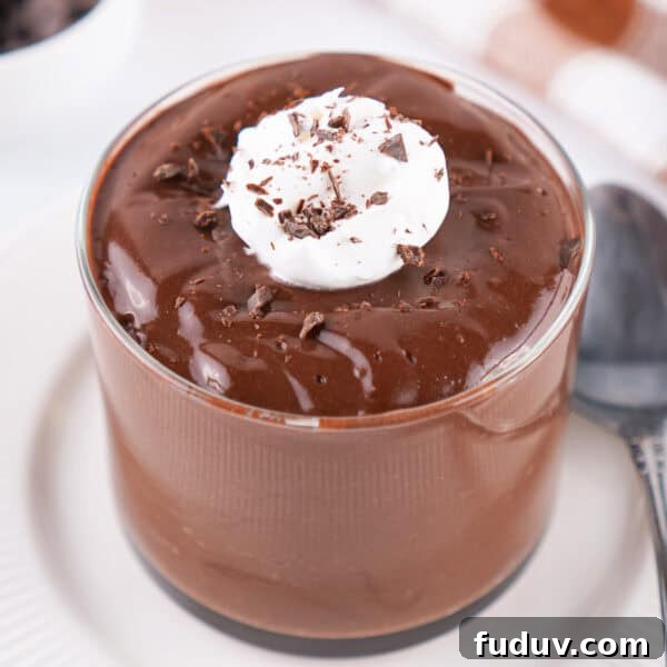 glass of chocolate pudding topped with whipped topping and chocolate shavings on a white plate