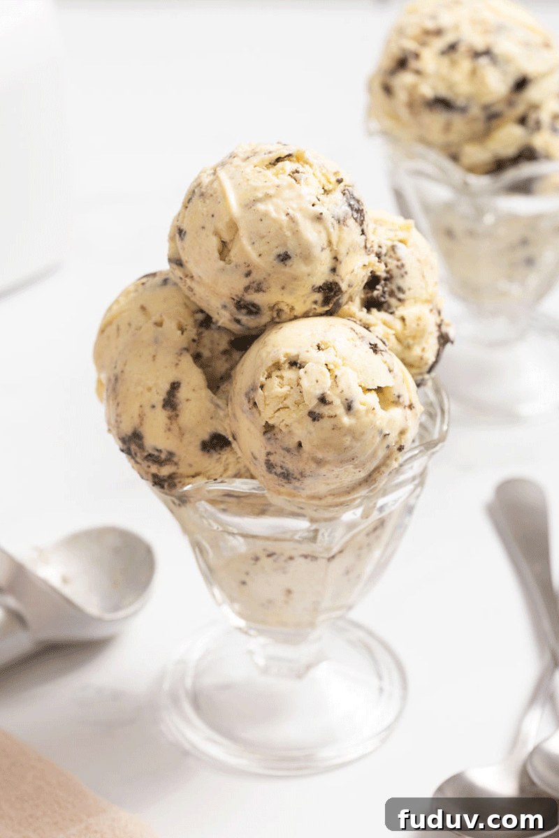 A glass ice cream sundae dish with 3 scoops of cookies and cream ice cream in it