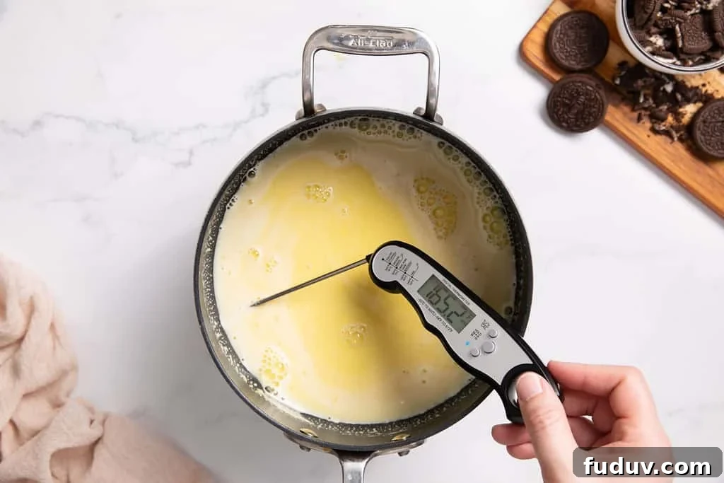 A saucepan with combined egg yolks, sugar and milk with scraped vanilla bean. A thermometer is in it to read the temperature.