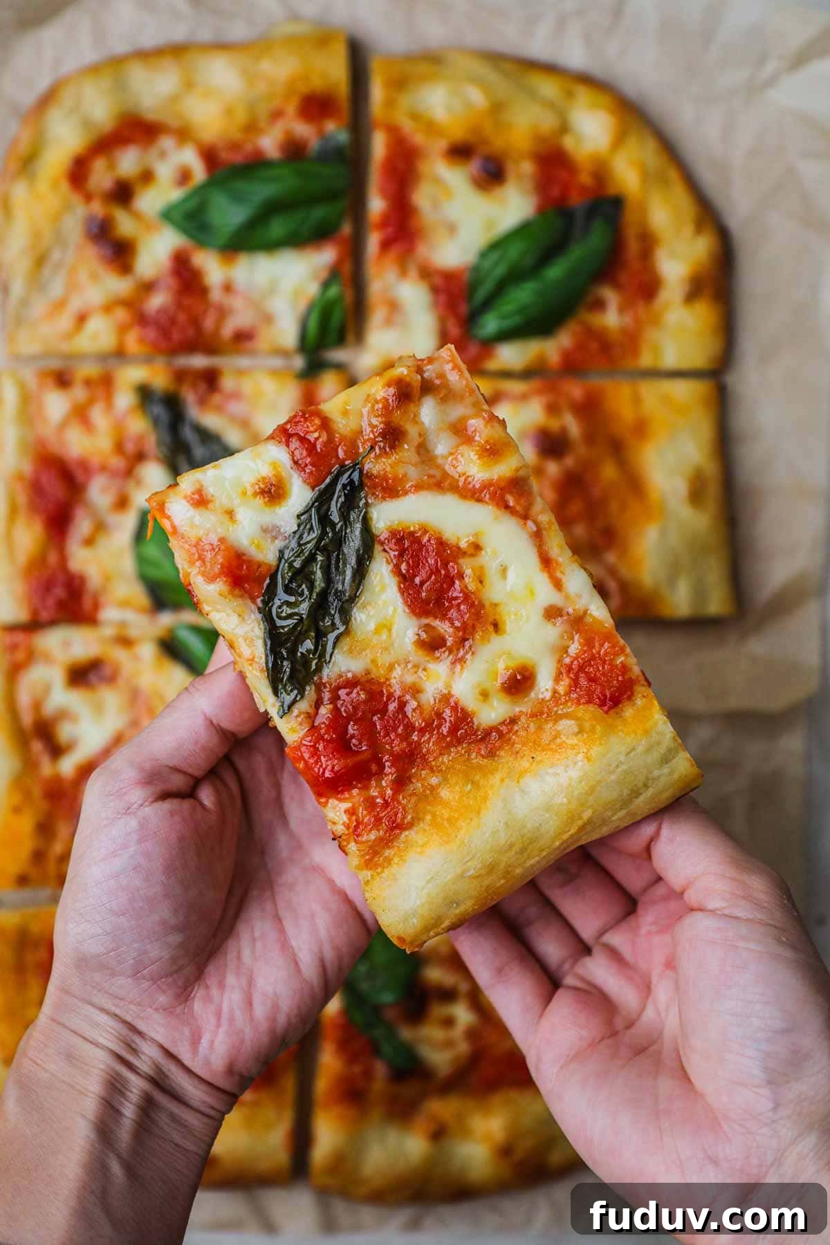 Hand holding a slice of homemade margherita pizza.