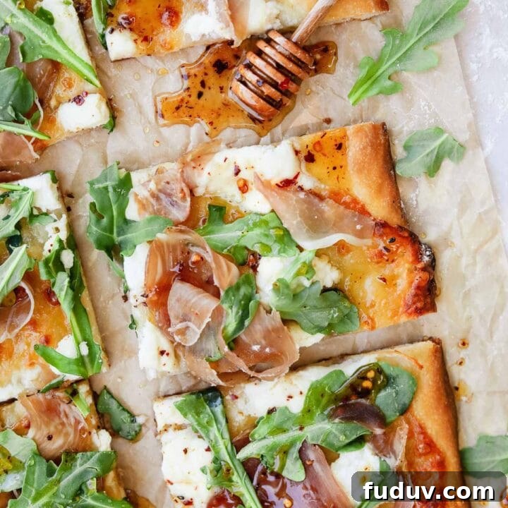 Prosciutto ricotta pizza with arugula and hot honey on parchment paper with honey dripper.