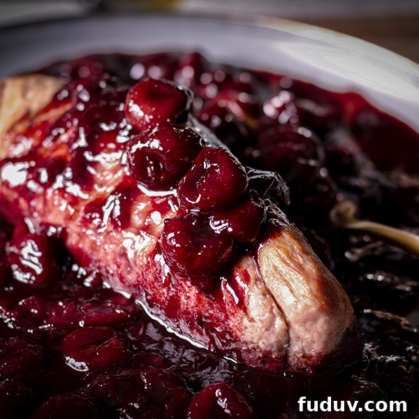 Roasted pork tenderloin on a plate covered in red wine cherry sauce.