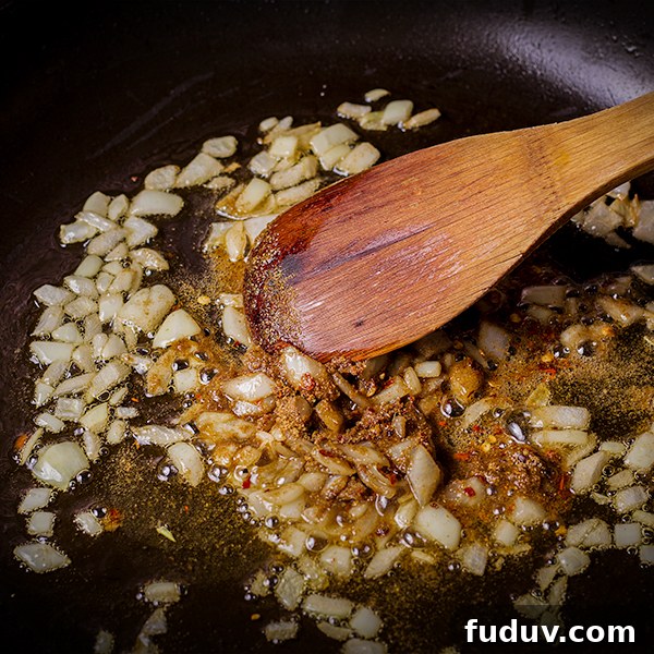 Stirring chopped onions and spices in a skillet.