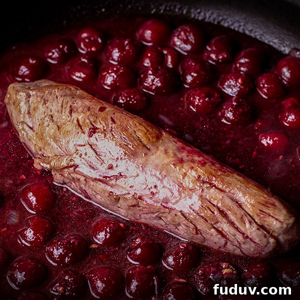 A pork tenderloin in a skillet with red wine cherry sauce.