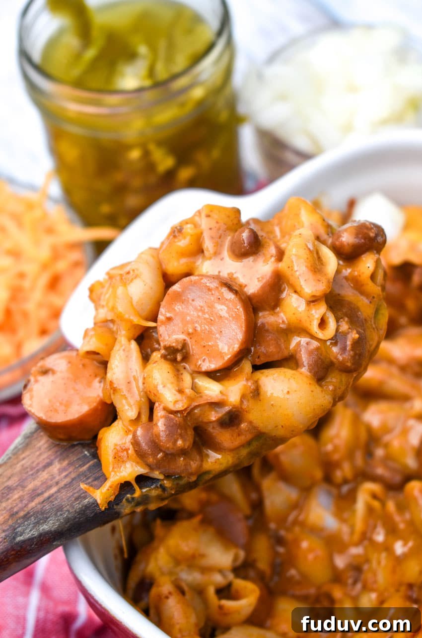 Chili Dog Mac & Cheese from a Box — Quick Classic Recipe 5 a wooden spoon holding up a scoop of chili dog mac and cheese with hot dogs