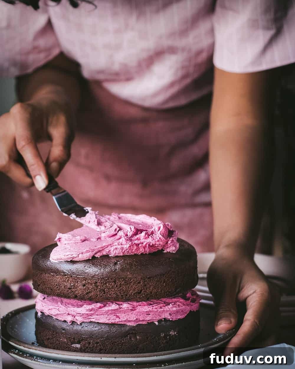 Woman smoothing frosting onto top of cake sitting on two stacked plates on a table.