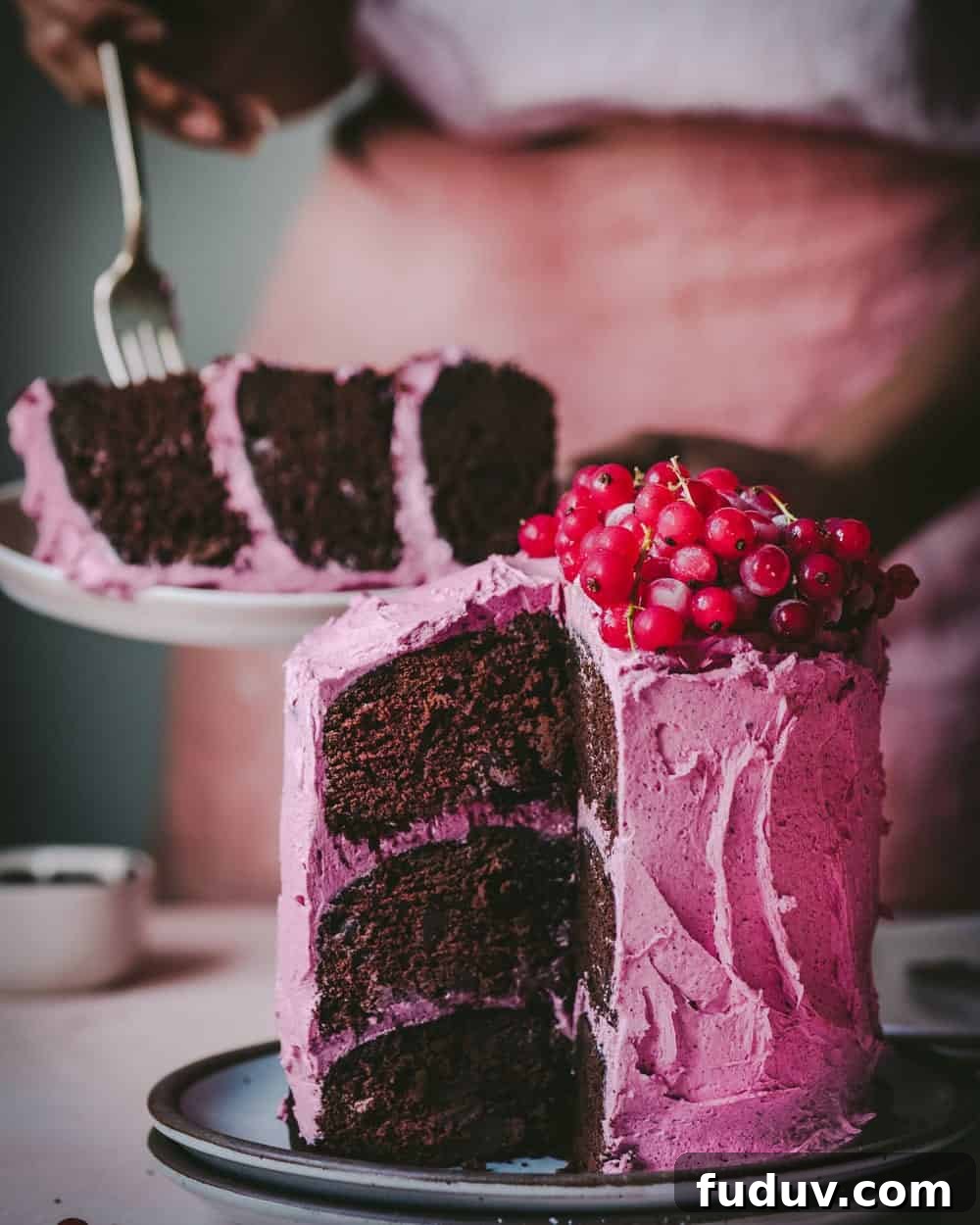Woman digging into a slice of cake on a plate behind the cake on table.