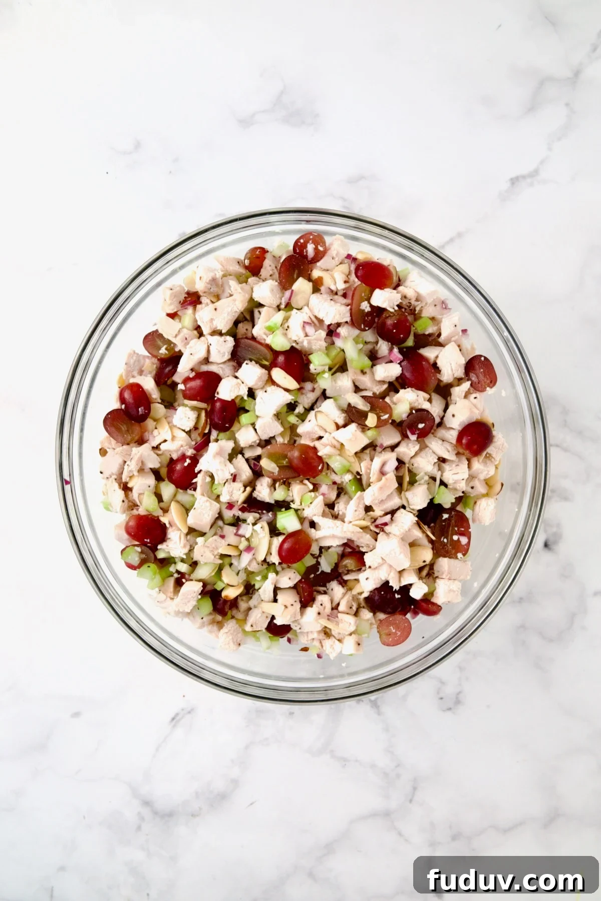 Chicken salad ingredients mixed together in glass bowl.